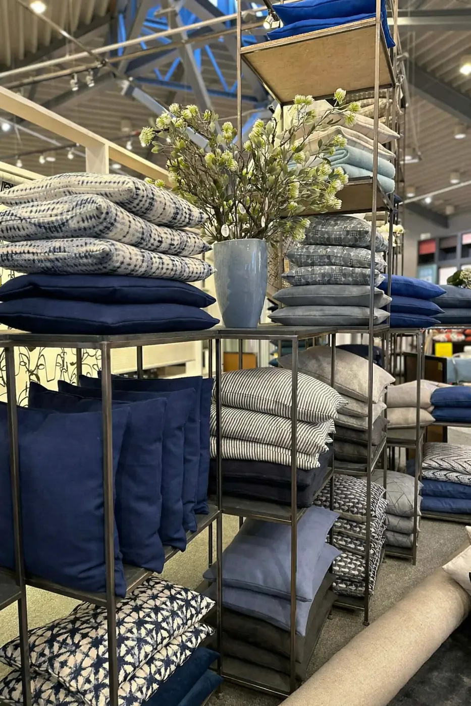 Reol med puder i støvede farver, vaser og blomstergrene